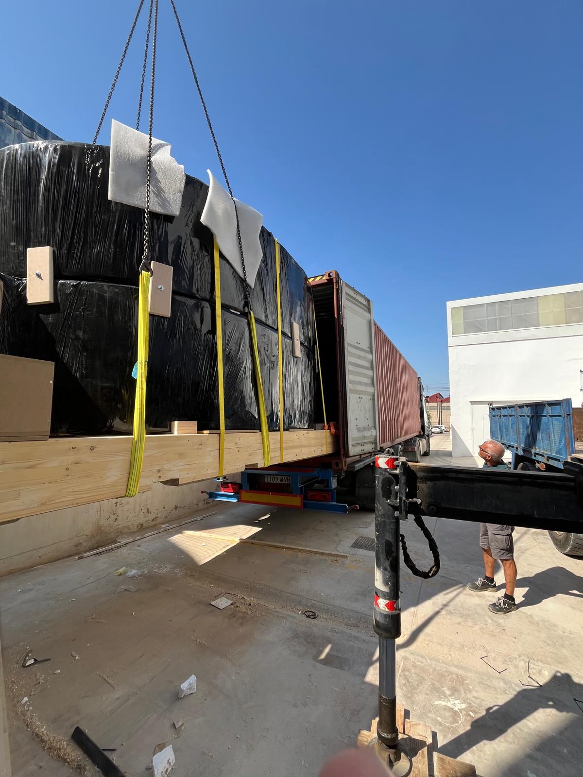 Wrapped sculpture sections slung on yellow straps beside the open container