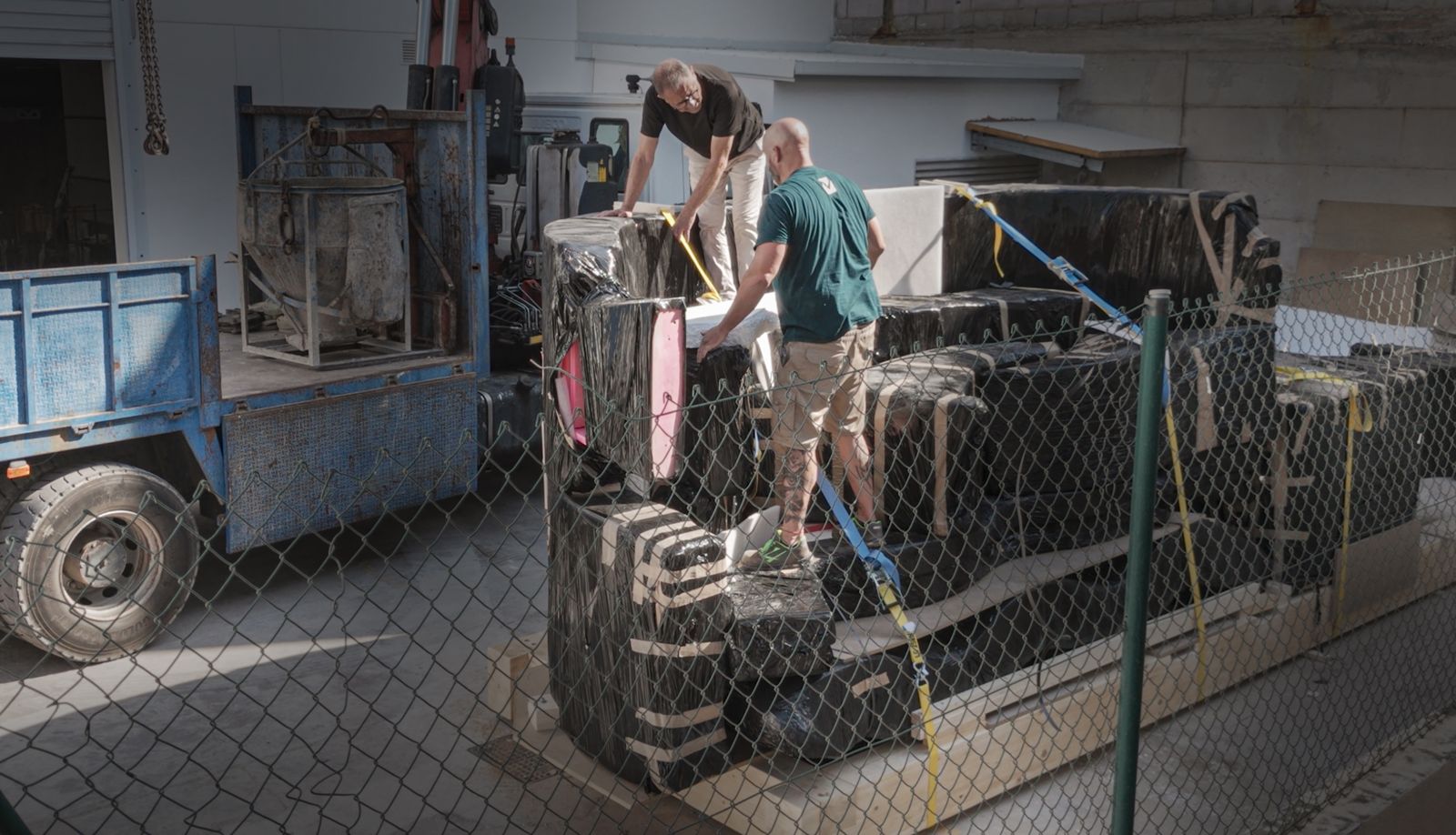 Team securing black-wrapped elements onto timber crating before loading