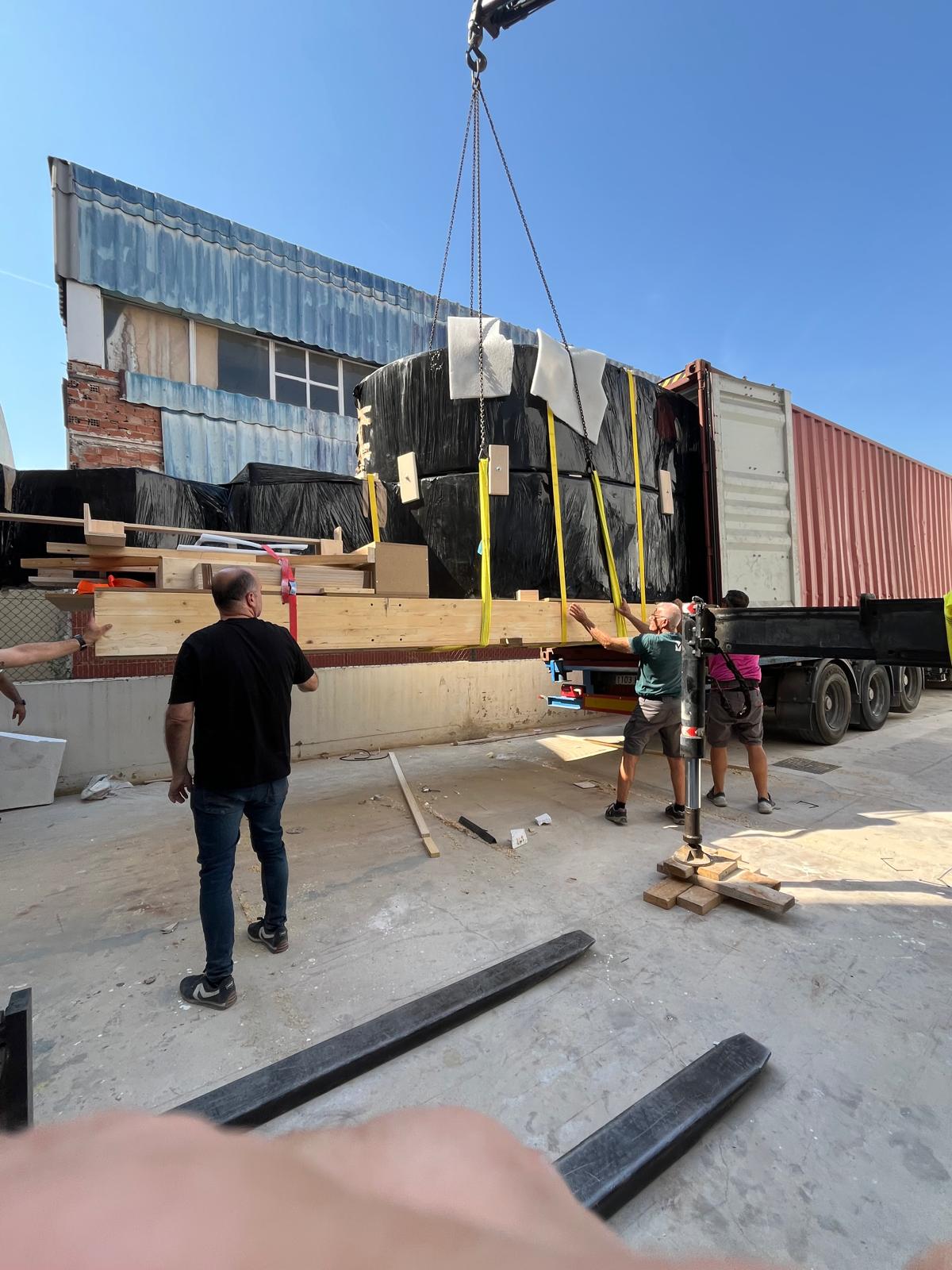 Crew guiding a wrapped Correfoc component craned toward the shipping container in Valencia