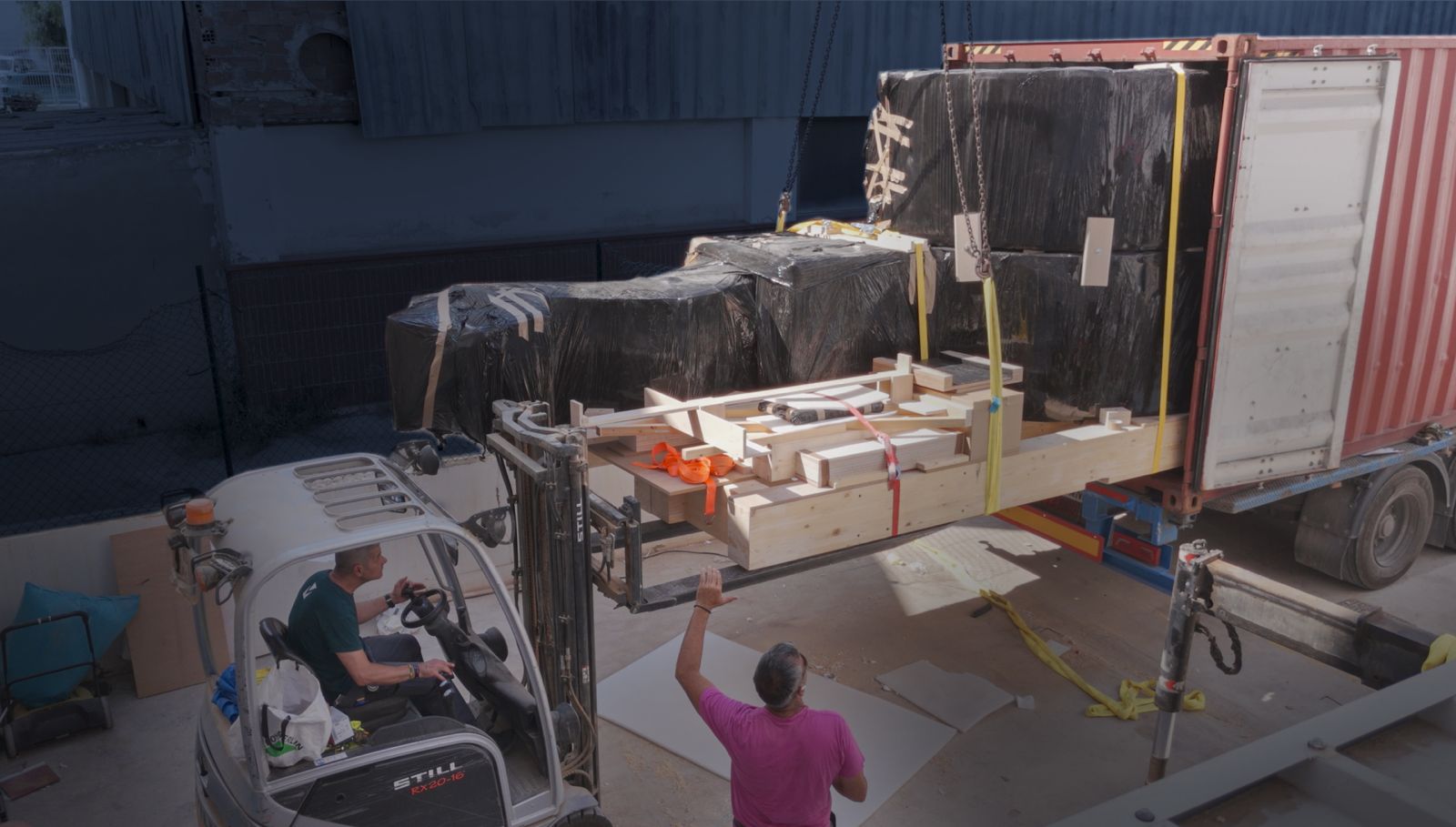 Forklift and crane easing a crated section into the container